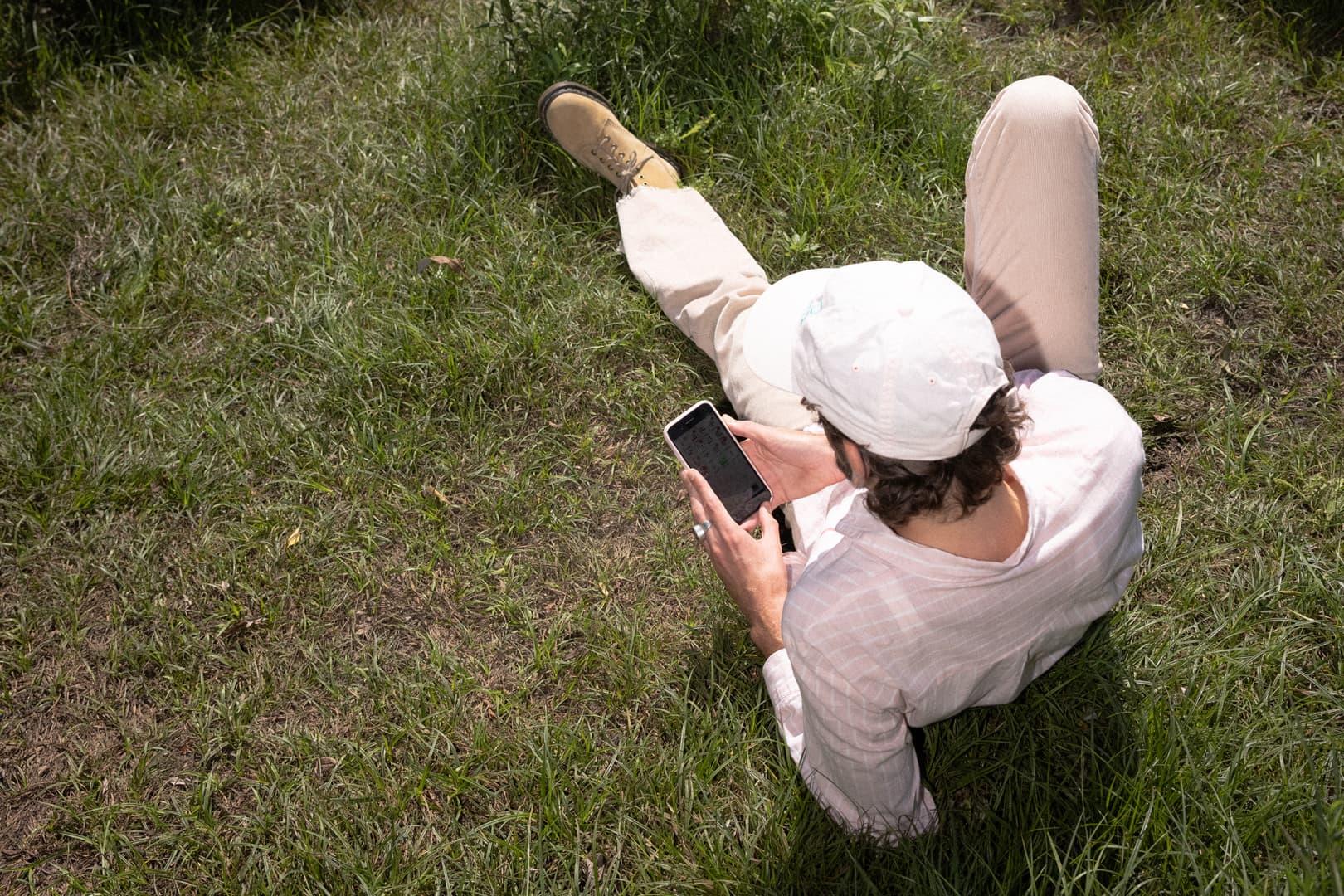 Man som ligger på en gräsmatta med en mobil i handen.